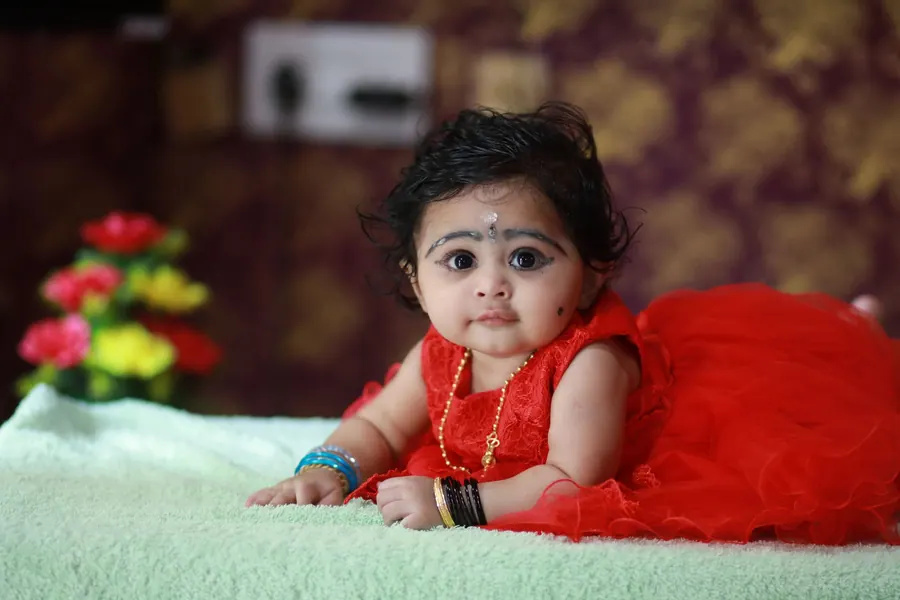 Baby in a red dress sitting up on the grass during a milestone session