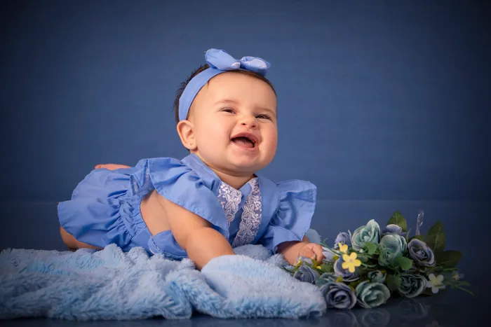 Baby in a blue outfit smiling up from a soft blanket