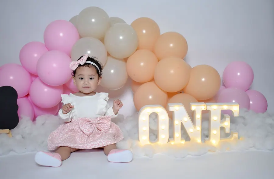 One-year-old seated in front of a balloon arch and a ONE sign in the studio