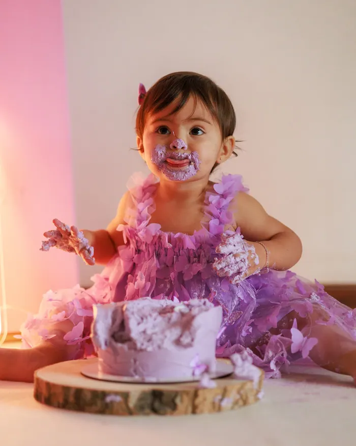 Toddler in a tulle dress reaching into her first birthday cake during a cake smash session