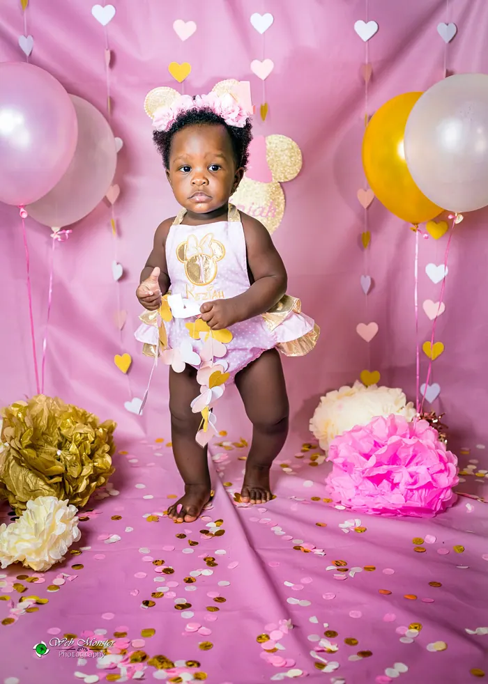 Toddler in a party dress beside her first birthday cake