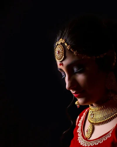 Close profile of the bride in low light, showing her nath and maang tikka