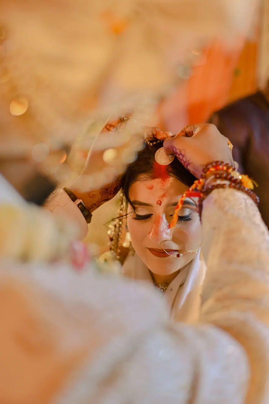 Bride with her eyes lowered as the sindoor is applied, close in on her face