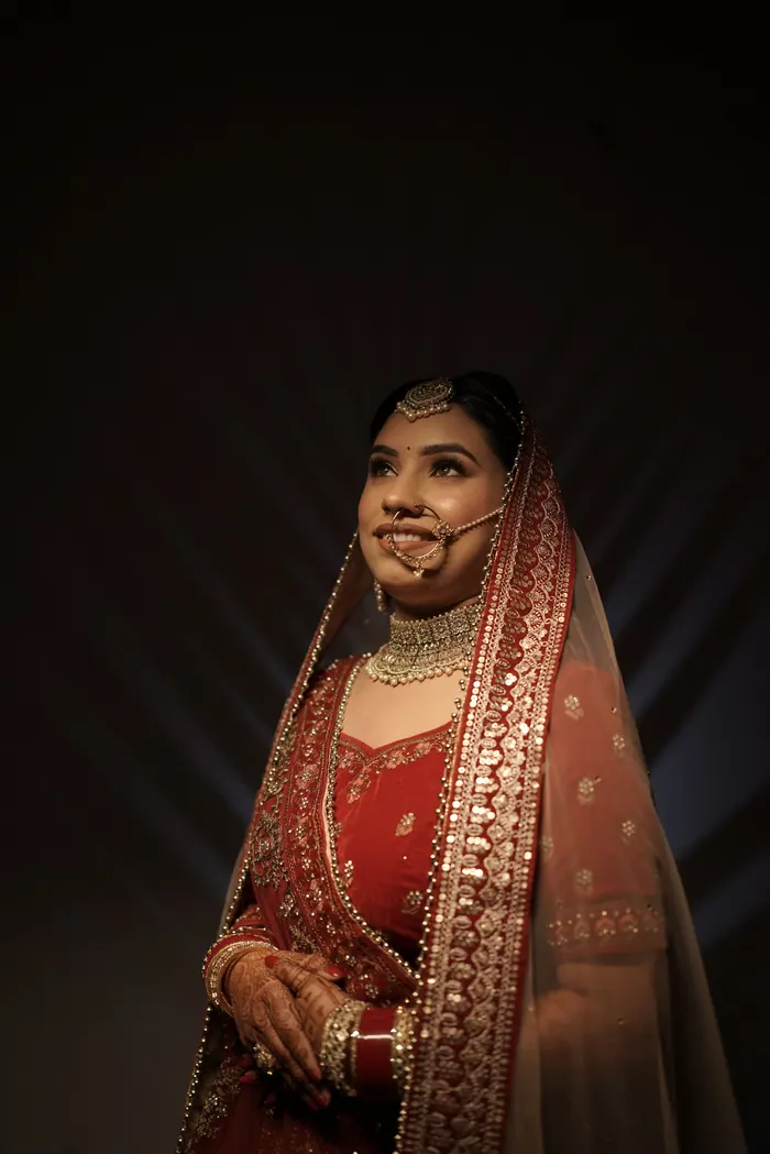 Bridal portrait under a red veil, gold jewellery catching the window light