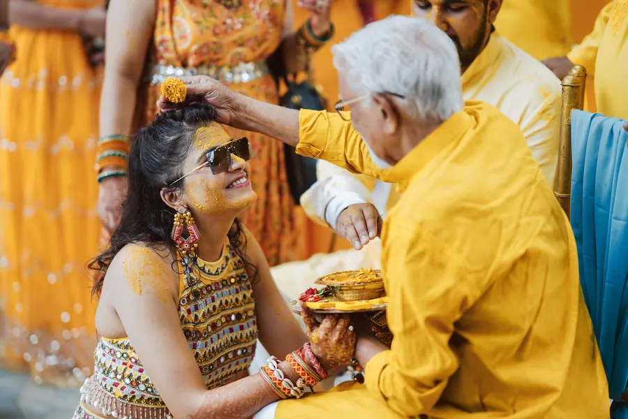 An older relative feeding the groom during the haldi, both of them laughing
