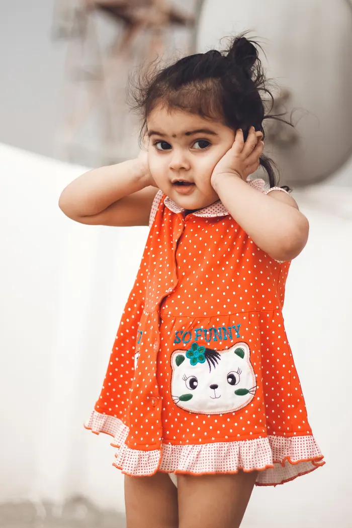 Small child in an orange dress covering her face during a studio session