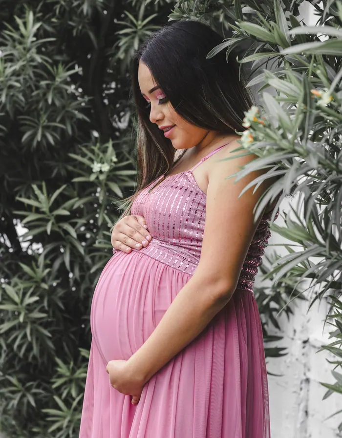 Expectant mother outdoors among greenery in a pink drape