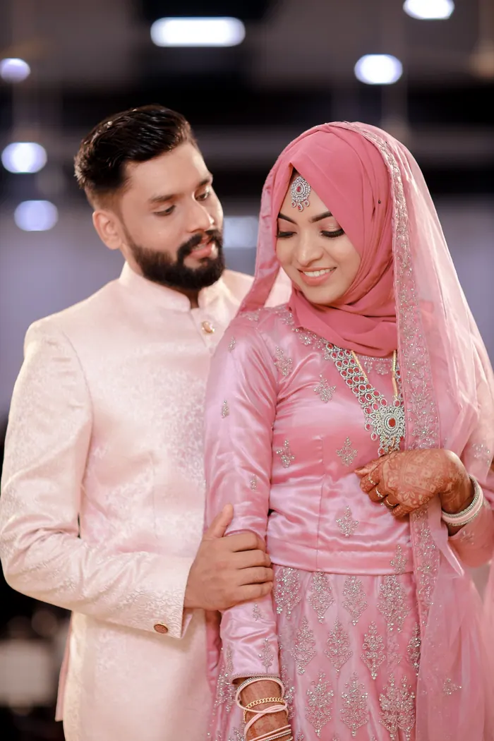 Bride and groom in pale pink after the nikah, photographed against a plain wall