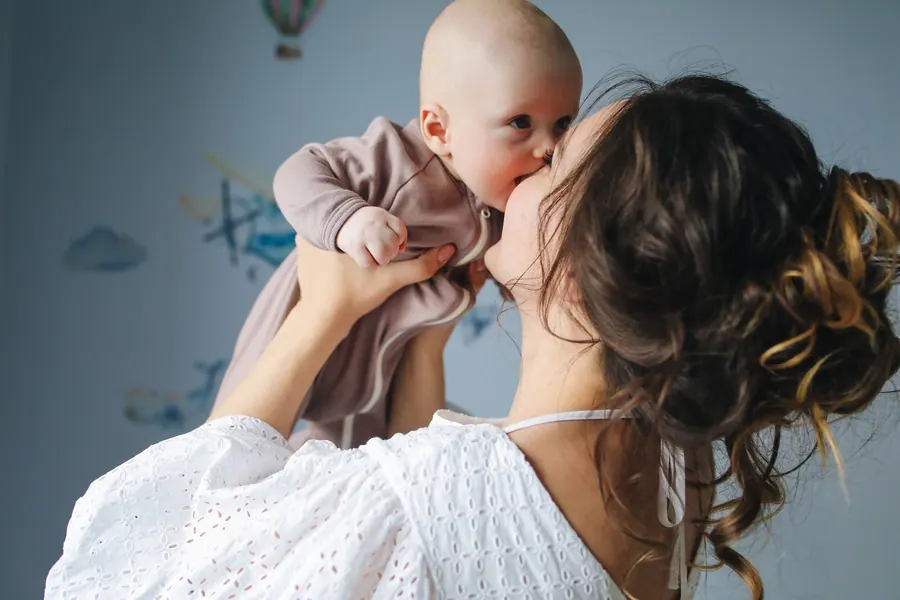 Mother holding her newborn close, soft window light behind them