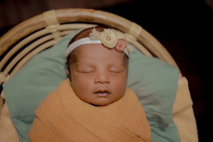 Newborn settled in a woven basket with a knitted headband