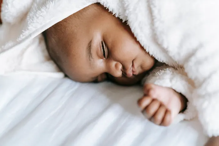 Newborn asleep on a white blanket, one hand open beside the face