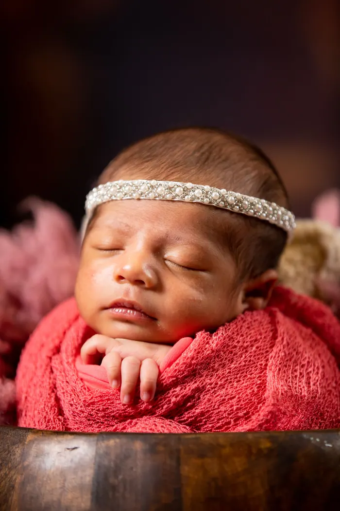 Newborn asleep in a pink wrap with a knitted headband